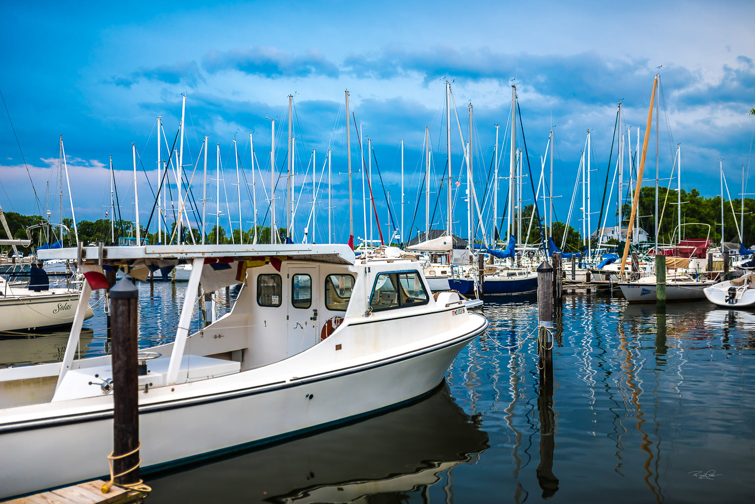 The Heart of Solomons — A white workboat docked at Zahniser's Marina in Solomons Island, surrounded by a forest of sailboat masts under a deep blue, cloud-filled sky.